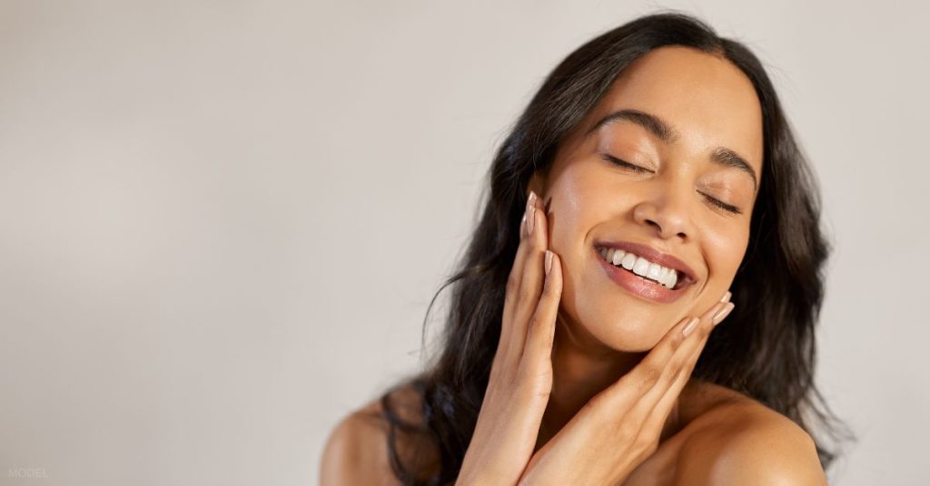 Smiling woman with her eyes closed and hands on her cheeks (model)