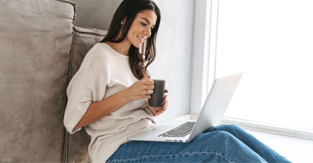 Beautiful woman looking at computer and holding coffee mug (model)